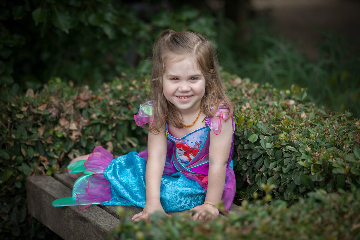 Girl sitting in the Ariel shimmer dress with purple bodice and teal glitter mermaid skirt